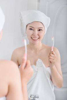 woman in bath towel brushing teeth with mirror in the bathroom