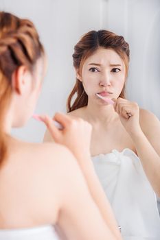 unhappy woman in bath towel brushing teeth with mirror in the bathroom