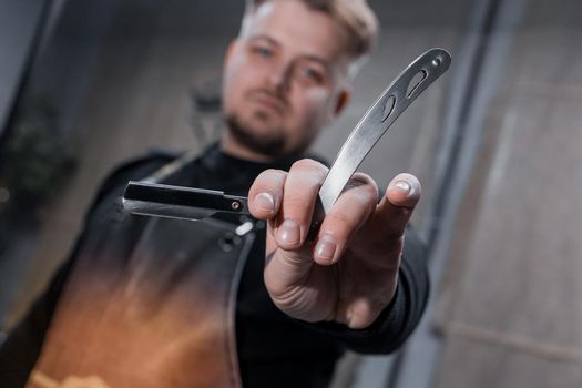 The hand of a barber or professional hairdresser holds a straight tool sharp razor equipment for shaving and beard care, close-up.