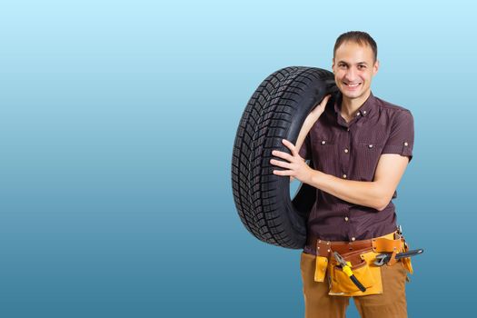 car mechanic carrying tire on blue background. happy man smiling amd looking into camera