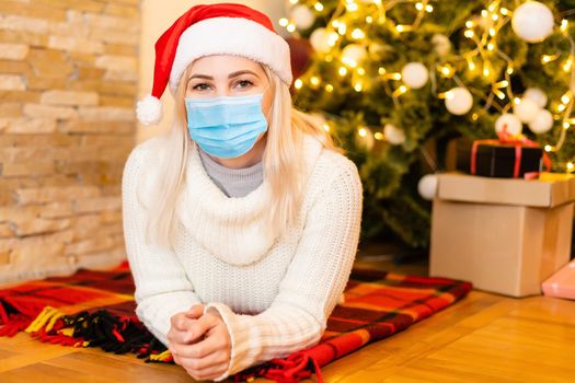 Christmas with coronawirus pandemic. Portrait of a young woman wearing protective face mask and looking sad for Covid-19 with Christmas tree on the background, coronavirus and Christmas concept.