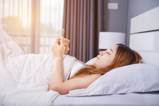 woman using her smartphone on bed in the bedroom with soft light