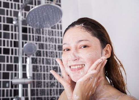 woman washing face in shower foaming in the bathroom