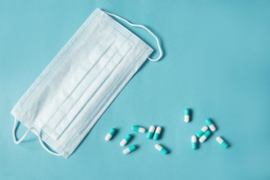 Respiratory mask and medicine in capsules on blue background.Virus prevention and treatment.
