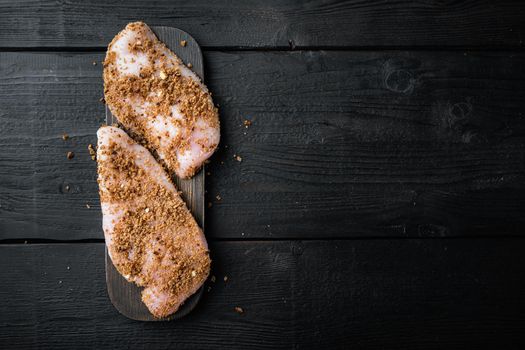 Crumbed uncooked chicken breasts ingredient, on black wooden background, flat lay with space for text