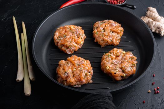 Raw fish patties with salmon fillet and lemongrass, on black textured background