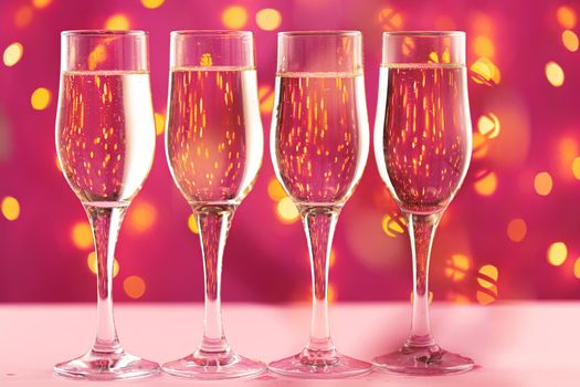 Four champagne glasses against pink background with blurred garland lights
