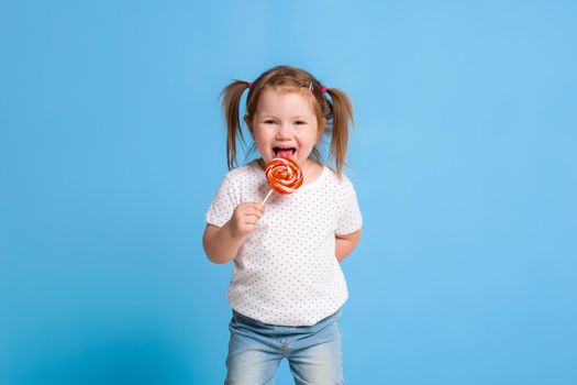 Beautiful little female child holding huge lollipop spiral candy smiling happy isolated on blue background. In children loving sweet and caramel concept