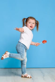 Beautiful little female child holding huge lollipop spiral candy smiling happy isolated on blue background. In children loving sweet and caramel concept