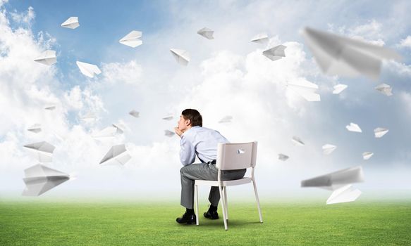 young businessman sits on an office chair, thoughtful and looking up