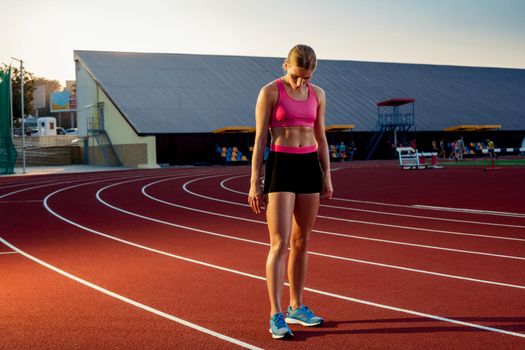 Picture of beautiful young European female runner or sprinter standing on outdoor stadium track, feeling exhausted after sprint or marathon. Jogging, sport, healthy active lifestyle concept.