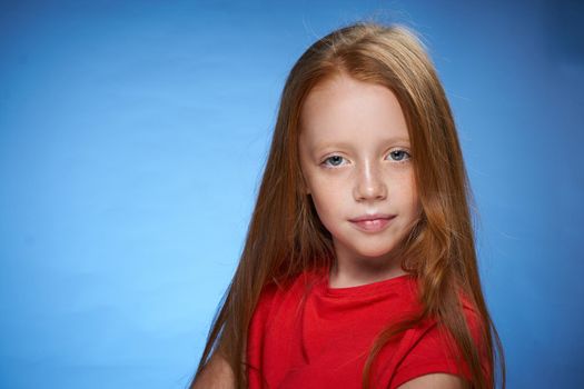 cute red-haired girl in red t-shirt emotions blue background. High quality photo