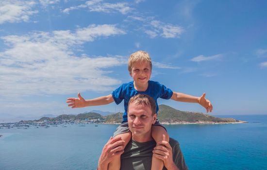 Front boy son laugh sitting on fathers shoulders. No photoshop sun on skin. Sea, clouds, island background. Funny photo, happiness lifestyle, Father's Day, love parenthood, family holiday concept.