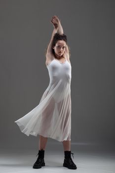 Girl with curly hair making ballet poses. Ballerina in white dress and black boots.