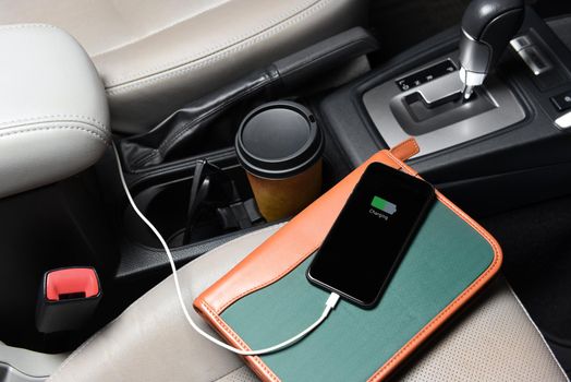 A businessman cell phone on the passenger seat and plugged into the cars charging port with coffee cup, and notebook.