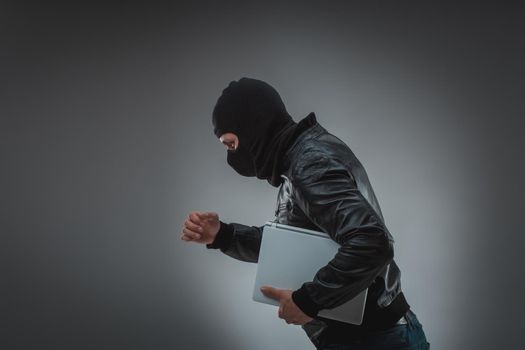 Thief stealing a laptop computer. Isolated on gray background. Studio shot