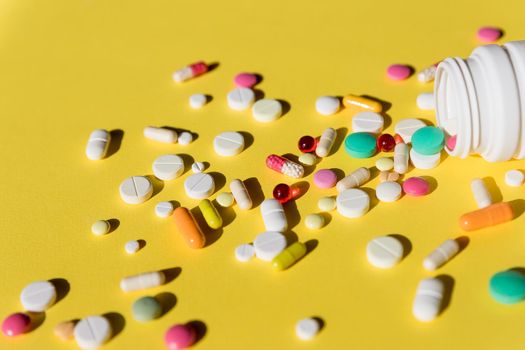 Pills spilling out of pill bottle isolated on yellow.