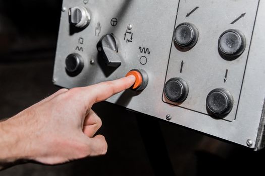 The worker's hand presses the red button on the old system and control panel of industrial equipment with his finger.