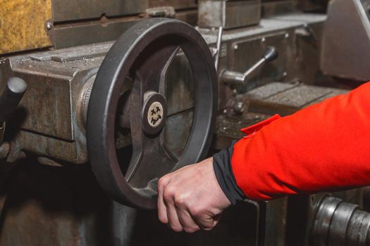 The hand of a man worker holds a special, steering wheel by the handle and controls the work of the milling machine in an industrial plant.