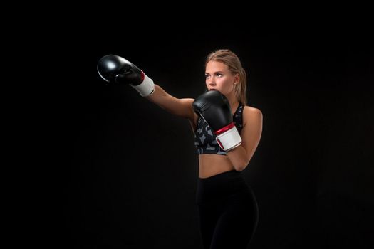 Beautiful female athlete in boxing gloves, in the studio on a black background. The boxer fulfills the blow