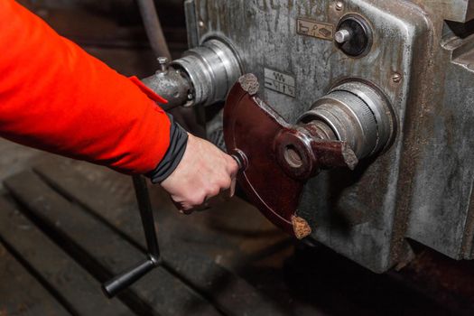 The hand of a man in a red work suit, holds on to the handle and controls the work of an old milling machine in an industrial plant.