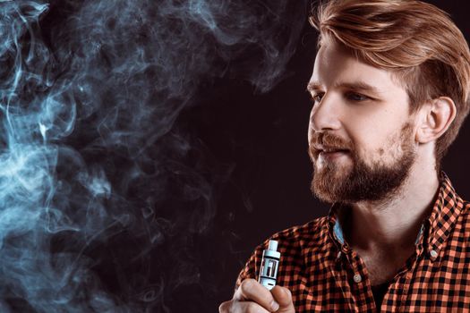 young man wearing a plaid shirt smokes an electronic cigarette on a black background. close-up