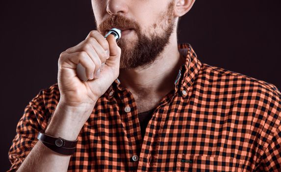 young man wearing a plaid shirt smokes an electronic cigarette on a black background. close-up