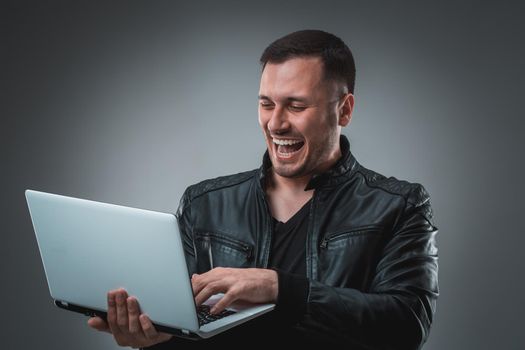 Happy man holding laptop on gray background. Portrait of a man in a black jacket in the studio