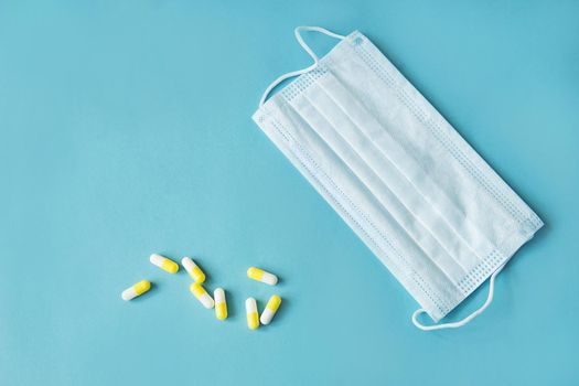 Respiratory mask and medicine in capsules on blue background.Virus prevention and treatment.