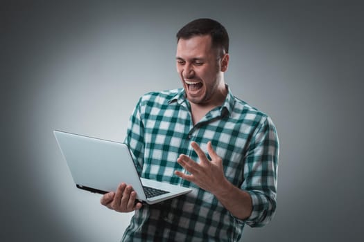 Attractive business man model in green shirt isolated on gray working with laptop, showing something by left hand. Caucasian guy.