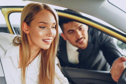 Man car dealer showing a woman buyer a new car in car salon