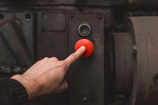 The worker's hand presses the red button on the old system of industrial equipment with his finger.