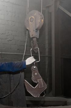 The hand of a working man takes a hook industrial lifting mechanism in the factory workshop.