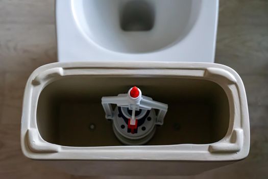 white toilet tank with an open lid and flush system. Plastic toilet drain system.