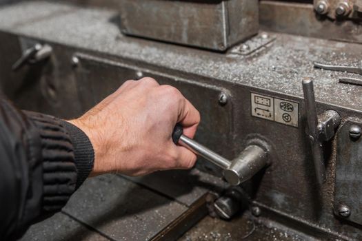 The hand of a man in a black work jumpsuit controls a milling machine by the handle for processing metal in an industrial enterprise.