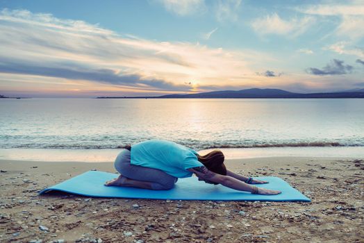 Young woman doing yoga exercise on summer beach near the sea in the morning, woman stretching her back