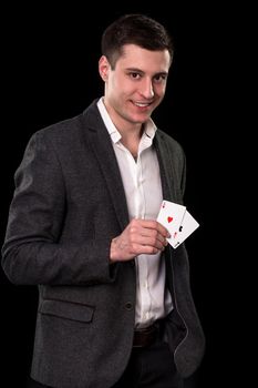 Young caucasian man in a dark suit and a white shirt holding two aces in his hand on black background. Gambling concept. Casino