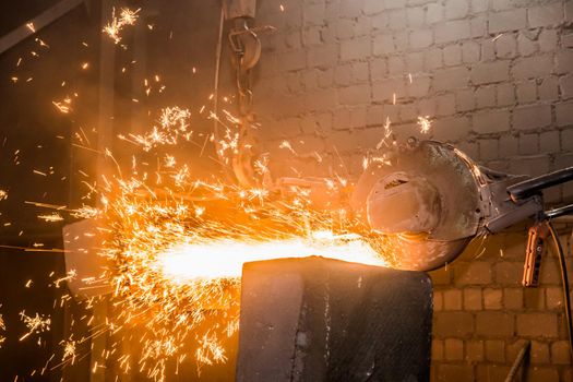 Heavy grinding equipment suspended on a chain with a hook processes and cleans cast iron reinforced concrete tubing in the workshop of an industrial plant.