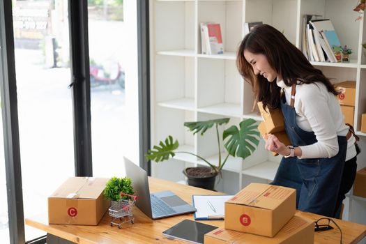 Start up small business entrepreneur SME or freelance asian woman using laptop with box, Young success Asian woman with her hand lift up , online marketing packaging box and delivery, SME concept