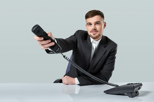 Portrait of attractive businessman holding telephone in his hand. This call is for you concept. A young man in a black suit dials the phone number while sitting in the office