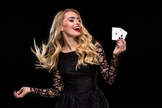 Beautiful young woman in black dress holding two ace of cards in her hand, isolated on black background. Poker. Casino. Roulette Blackjack Spin. Caucasian woman looking at the cards