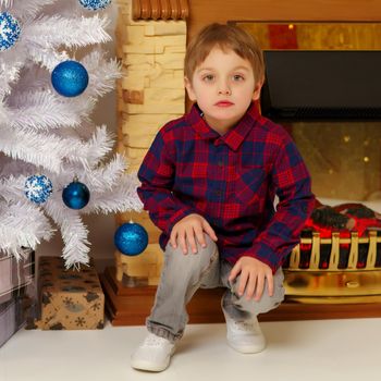 Cute little boy near the Christmas tree and fireplace in the new year. Family holidays concept.