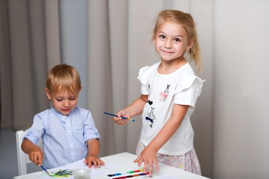 The boy and girl, brother and sister paint watercolors at the table on white sheets of paper. Concept aesthetic development of children, happy childhood.