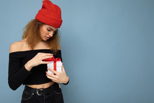 Beautiful happy young brunette woman isolated over colourful background wall wearing stylish casual clothes holding gift box and looking to the side. Copy space, mockup