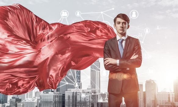 Young confident businessman wearing red cape against modern city background
