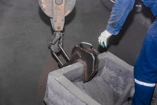 A man in overalls attaches an iron hook of a lifting mechanism to cast-iron tubing, reinforced concrete structures made of cast products at an industrial plant.