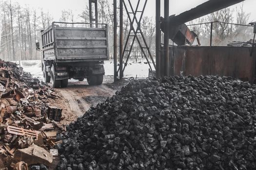 A dump truck at a landfill or on an industrial site unloaded a pile of coking coal from the body.