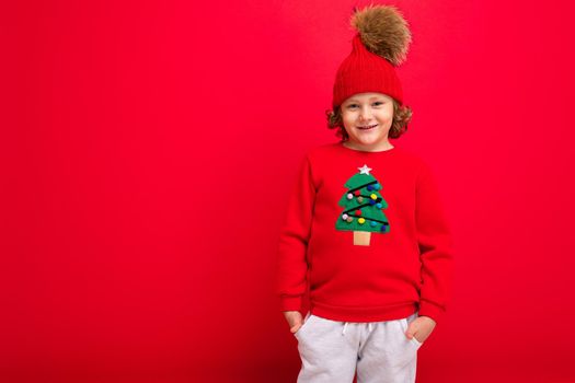 cool boy with curls on a red background in a sweater with a christmas tree.