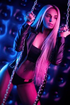the beautiful stylish fashionable girl in bodysuit posing in photo Studio on dark background with chains in neon light
