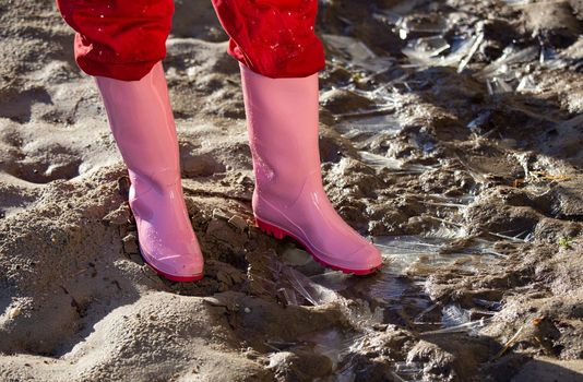 Close up of female legs in pink gumboots standing on frozen sandy ground